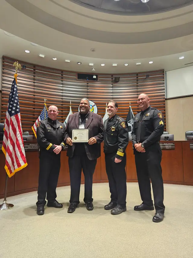 Carl Vinson standing with uniformed officers in a council chamber with flags and an award certificate